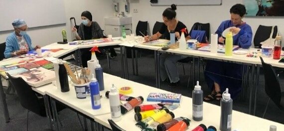 Farbraum_onkologisches_Kunstprojekt_Universitätsmedizin_Göttingen_Gruppe Das Bild ist im Rahmen des onkologischen Kunstprojektes "farbRaum" der Universitätsmedizin entstanden und zeigt diekreative Runde der Teilnehmer*innen. Die Tische sind übersäht von Malutensilien wie Farbtuben und Piinseln.