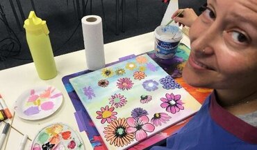 Farbraum_onkologisches_Kunstprojekt_Universitätsmedizin_Göttingen_Patientin_Blumenbild Auf dem Bild zu sehen ist eine Patienten im Rahmen des onkologischen Kunstprojektes Farbraum, die gerade ein farbenfrohes Bild mit vielen Blumen anfertigt und in die Kamera lächelt.